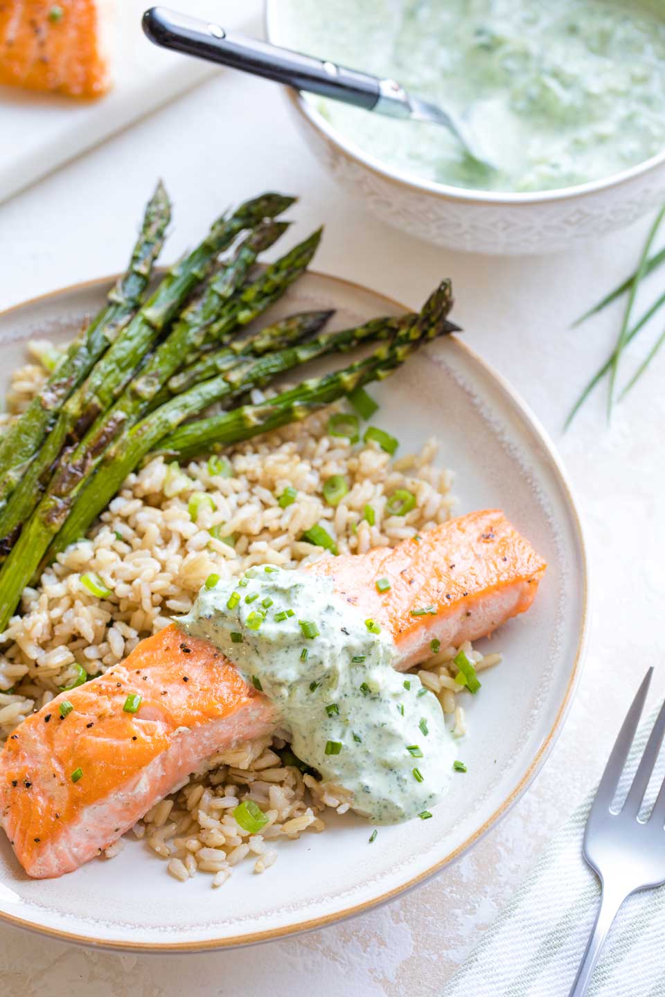 Overhead photo of the seared salmon, plated with brown rice and roasted asparagus, with a napkin, fork, and a bowl of extra tzatziki nearby.