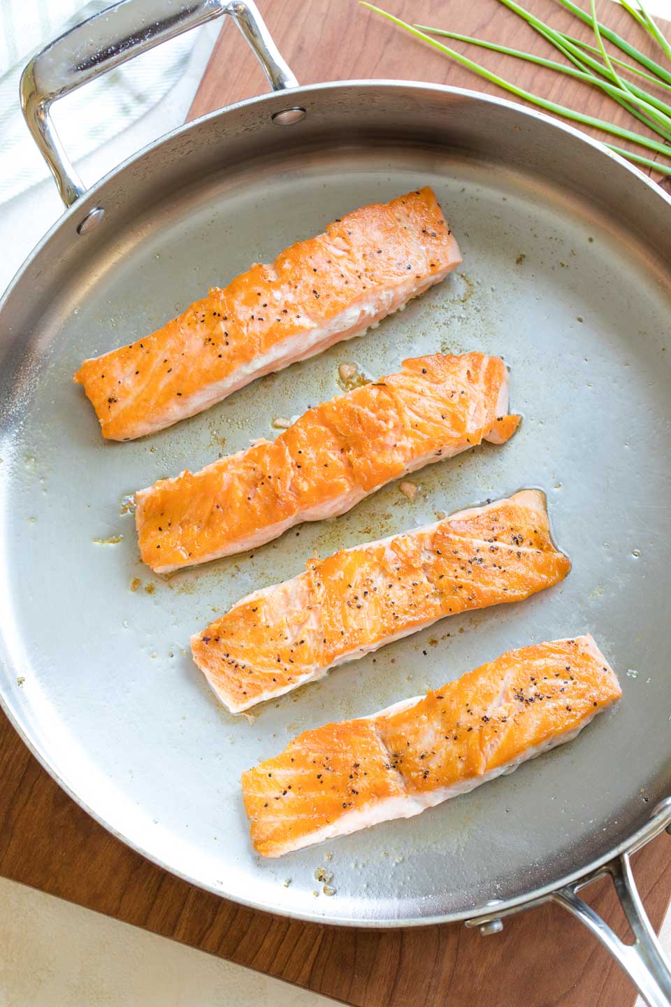Overhead of four salmon fillets in a metal pan after they have been seared on one side and then flipped, so you can see the seared top crust.