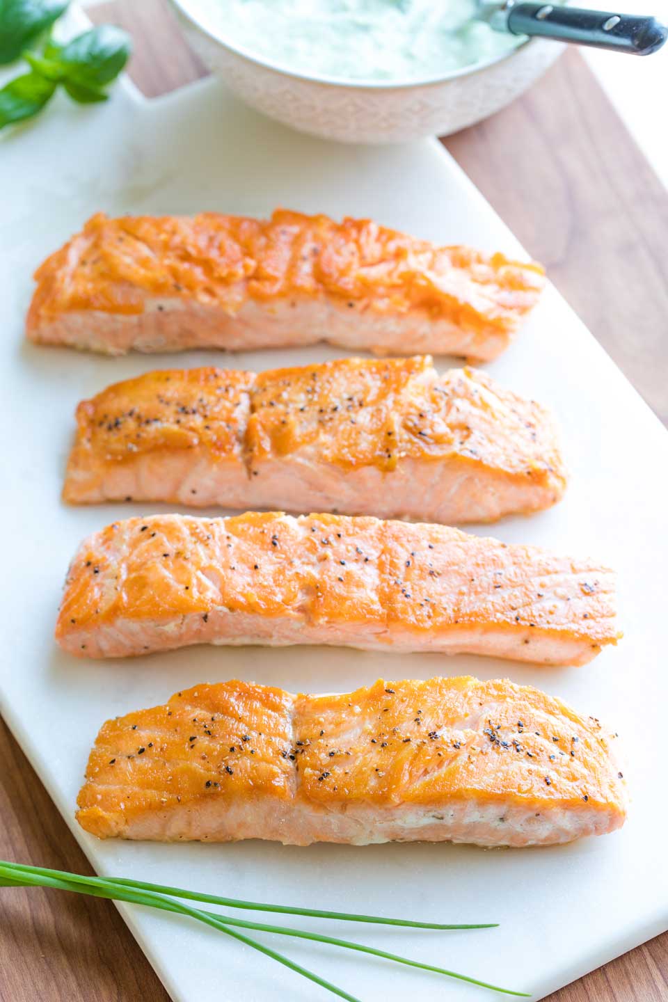 Four seared salmon filets after they've been removed from the fry pan, laying on a white marble serving slab before being served with sauce.