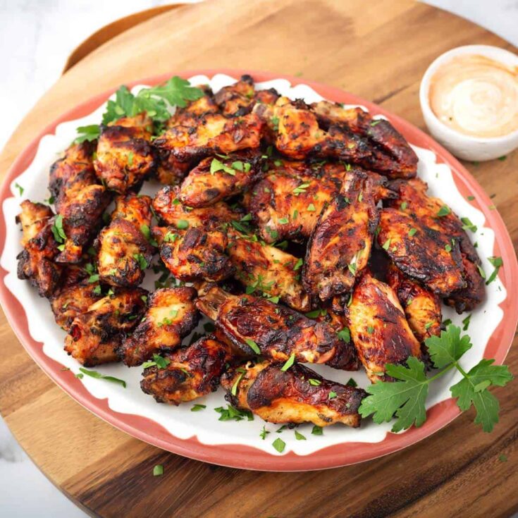 Overhead of a coral-colored serving platter piled with a batch of air fried chicken wings that are garnished with parsley.