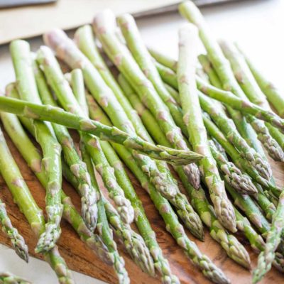 Pencil-width asparagus spears that are fresh and damp with water droplets, spilled across a cutting board.