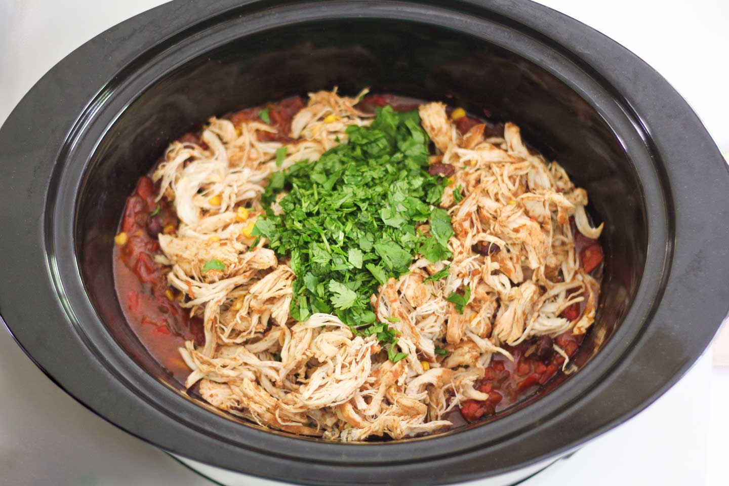 Overhead look into slow cooker showing chicken and other burrito bowl ingredients that are ready to be cooked.