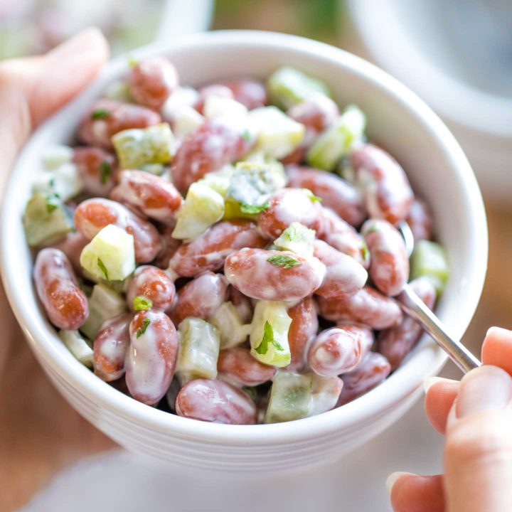 Overhead closeup of two hands cradling a bowl of Bean Salad, with the right hand holding a fork that's dipping in.