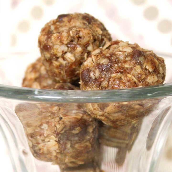 Closeup of a few of the finished energy balls in a glass parfait cup, with a polka-dot background lightly visible behind.