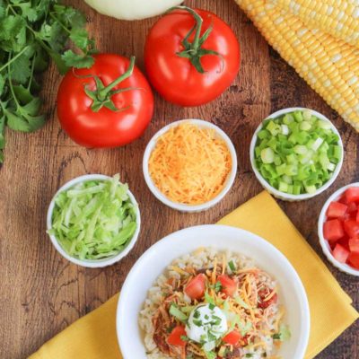 Overhead look onto table filled with fresh vegetables, burrito bowl toppings, and a vibrant bowl of slow cooker chicken.