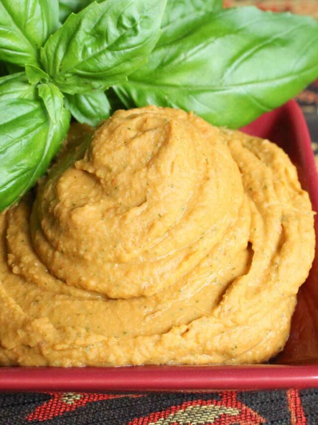 Table cloth set with a bowl full of white bean hummus and basil leaves.