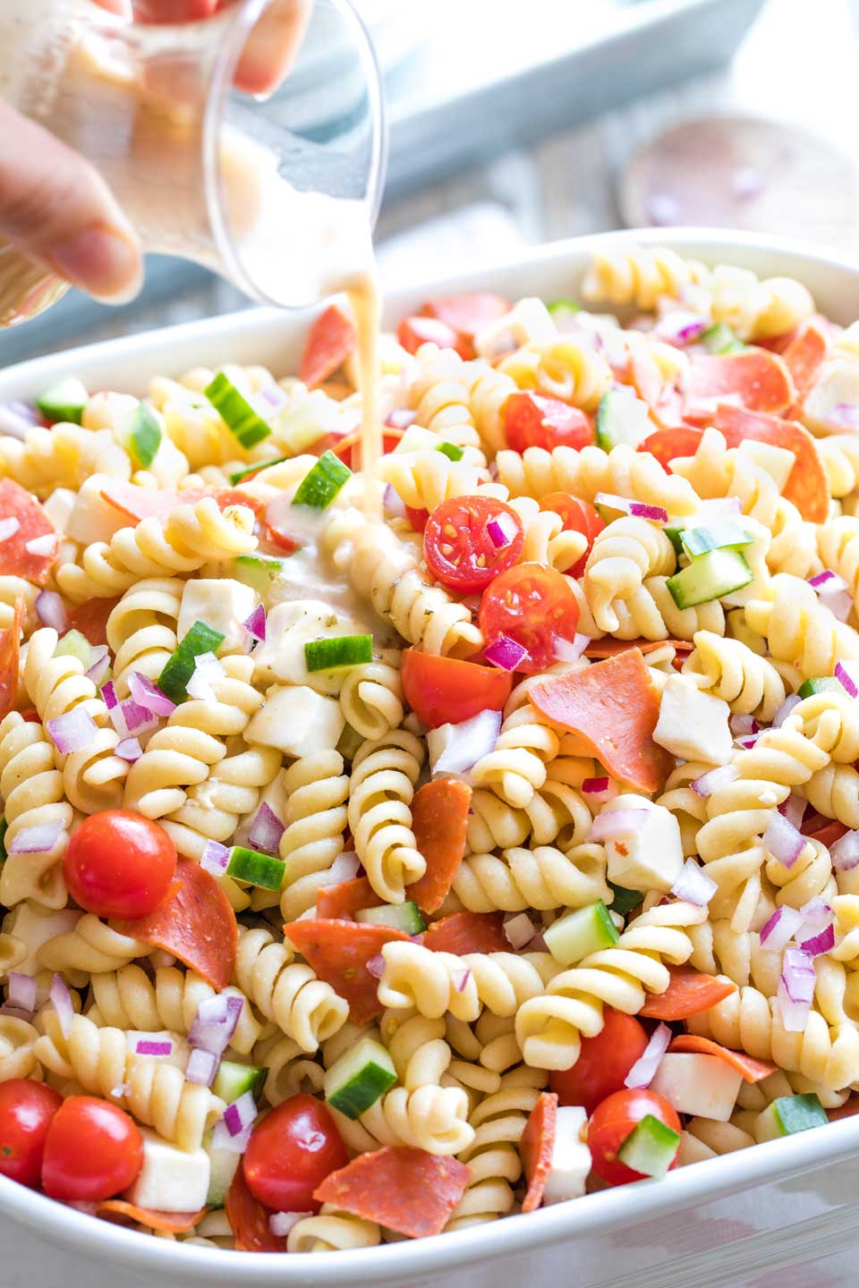 Closeup of the Italian dressing being poured over the mixed-together rotini pasta salad.