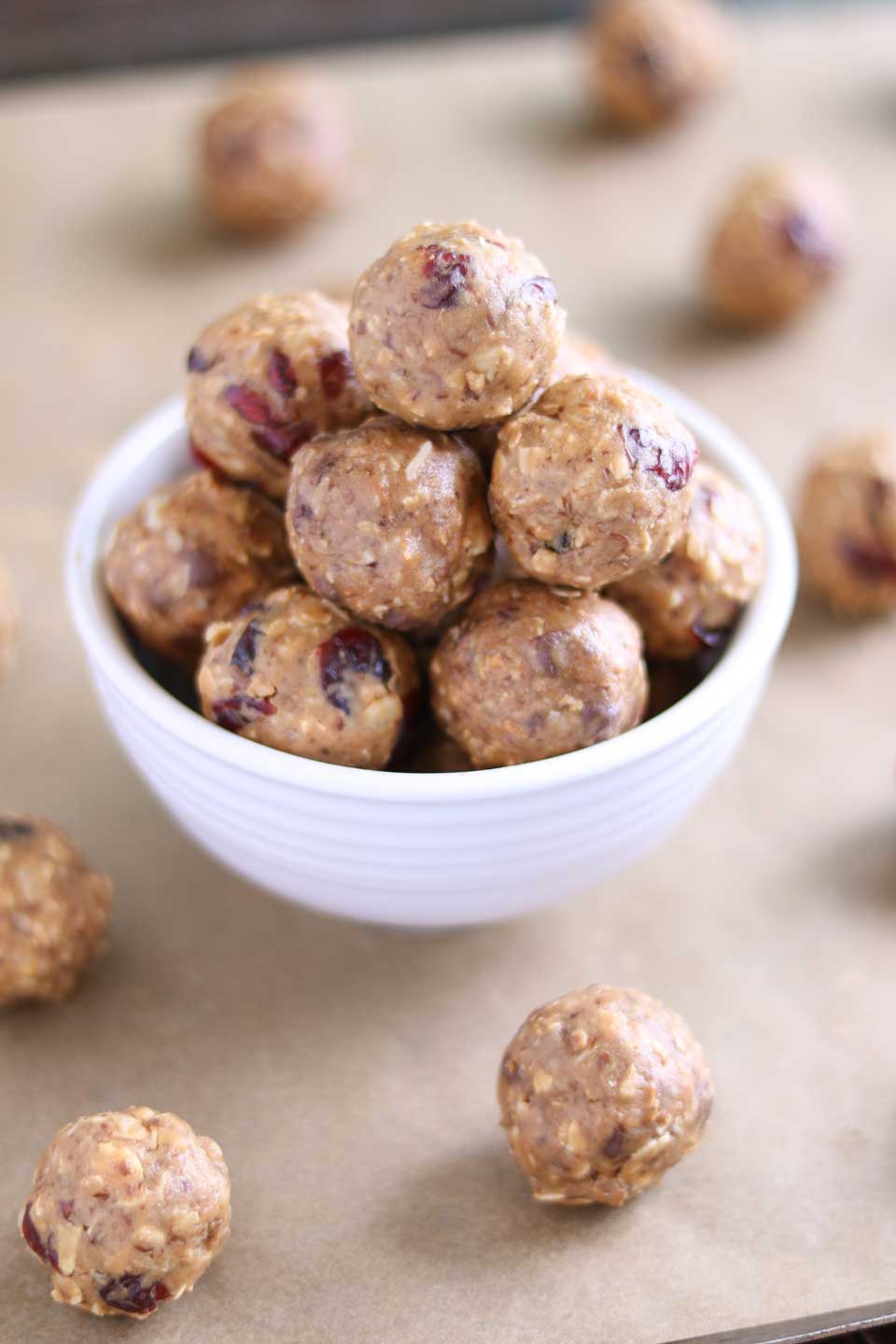 A white bowl piled with energy balls, with additional balls spread around it on brown parchment.