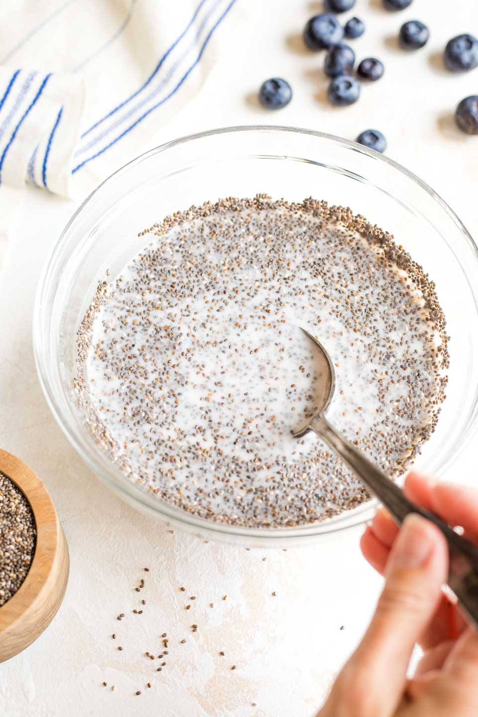 Hand holding spoon that's mixing up the chia pudding before chilling overnight.