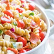 Closeup of the right side of a white serving bowl full of this pasta salad with forks and a red-striped cloth in the background..