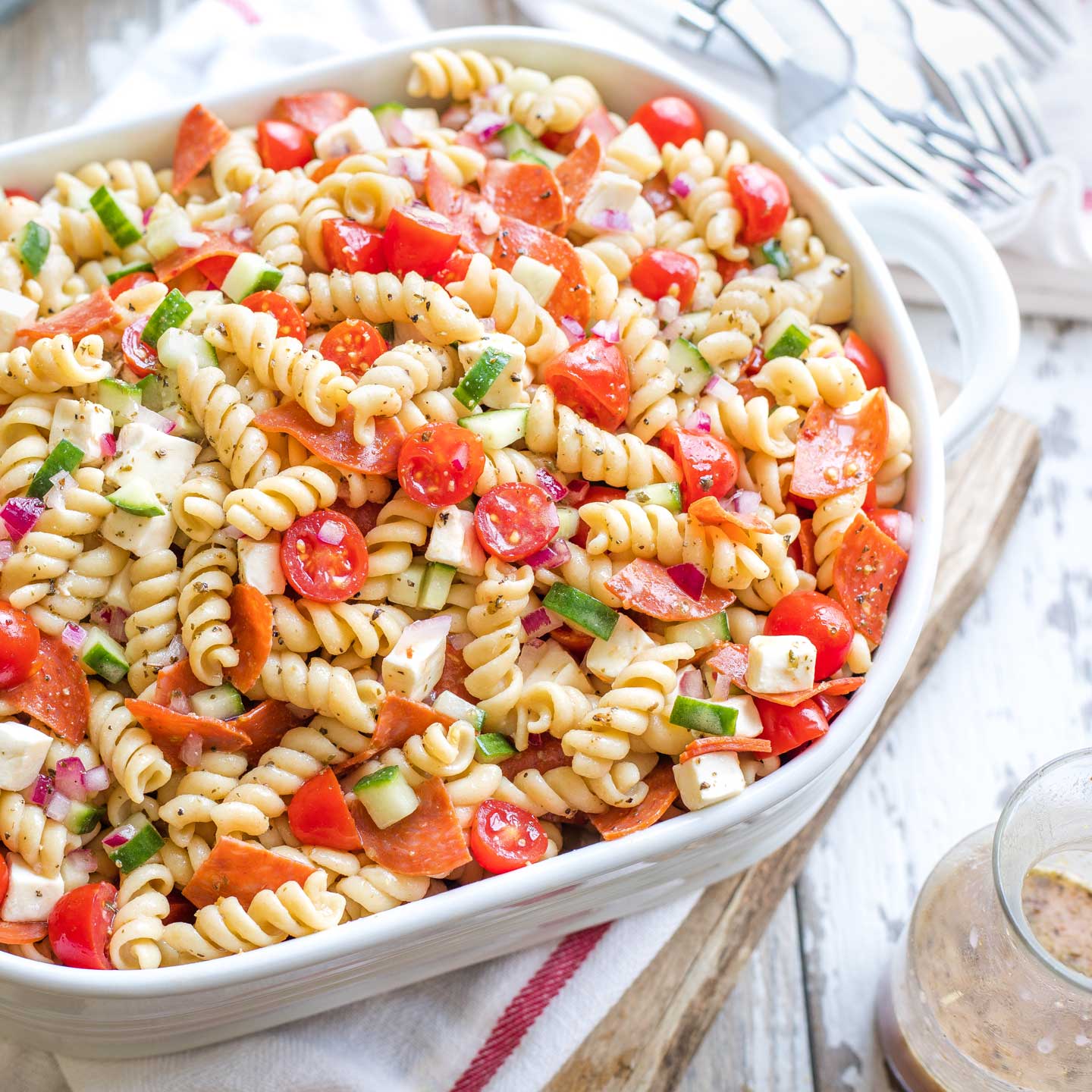 Overhead of a large oval serving dish piled with pasta salad, with a cruet of extra Italian dressing nearby.
