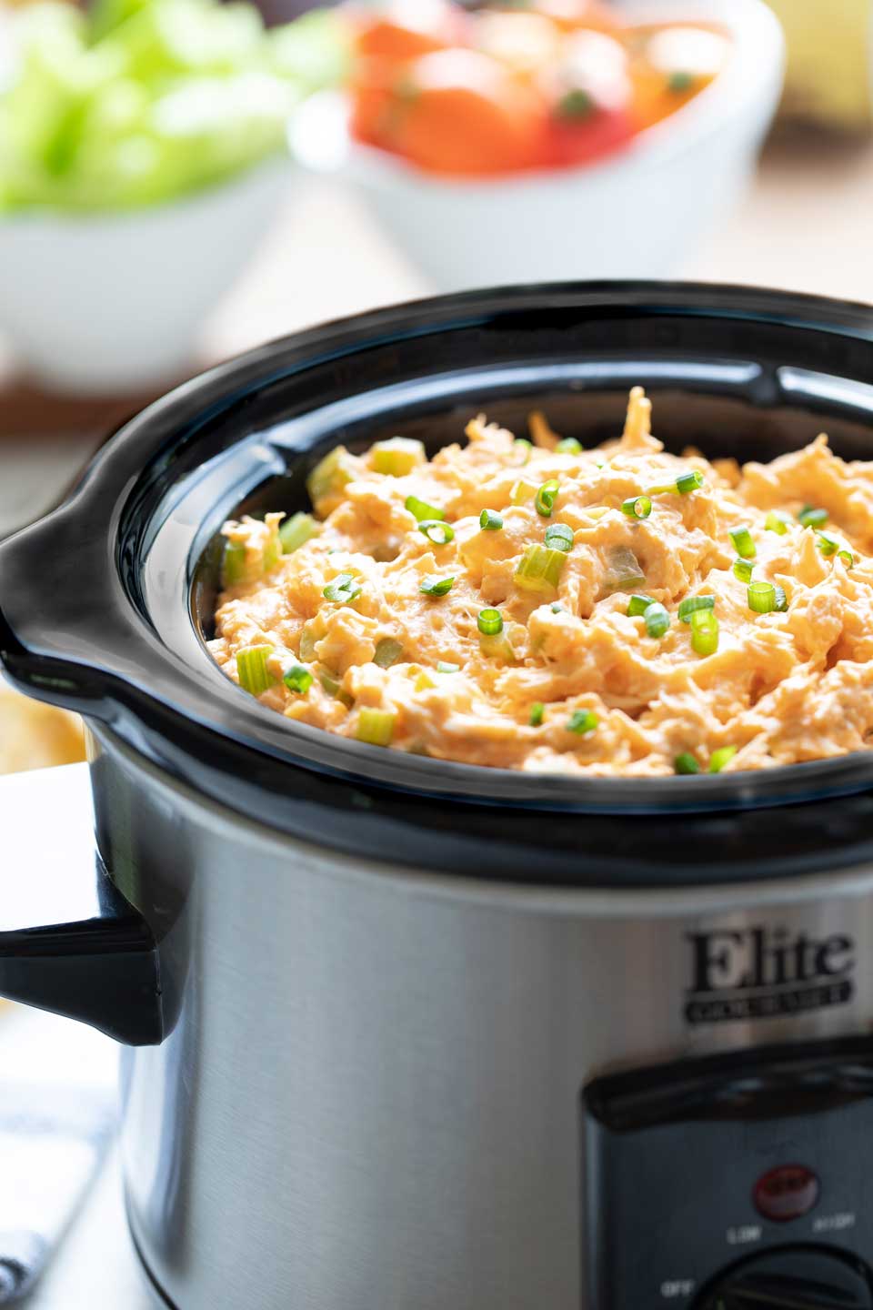 Side shot of appetizer-sized crockpot full of buffalo chicken dip, cooked and garnished with scallions.