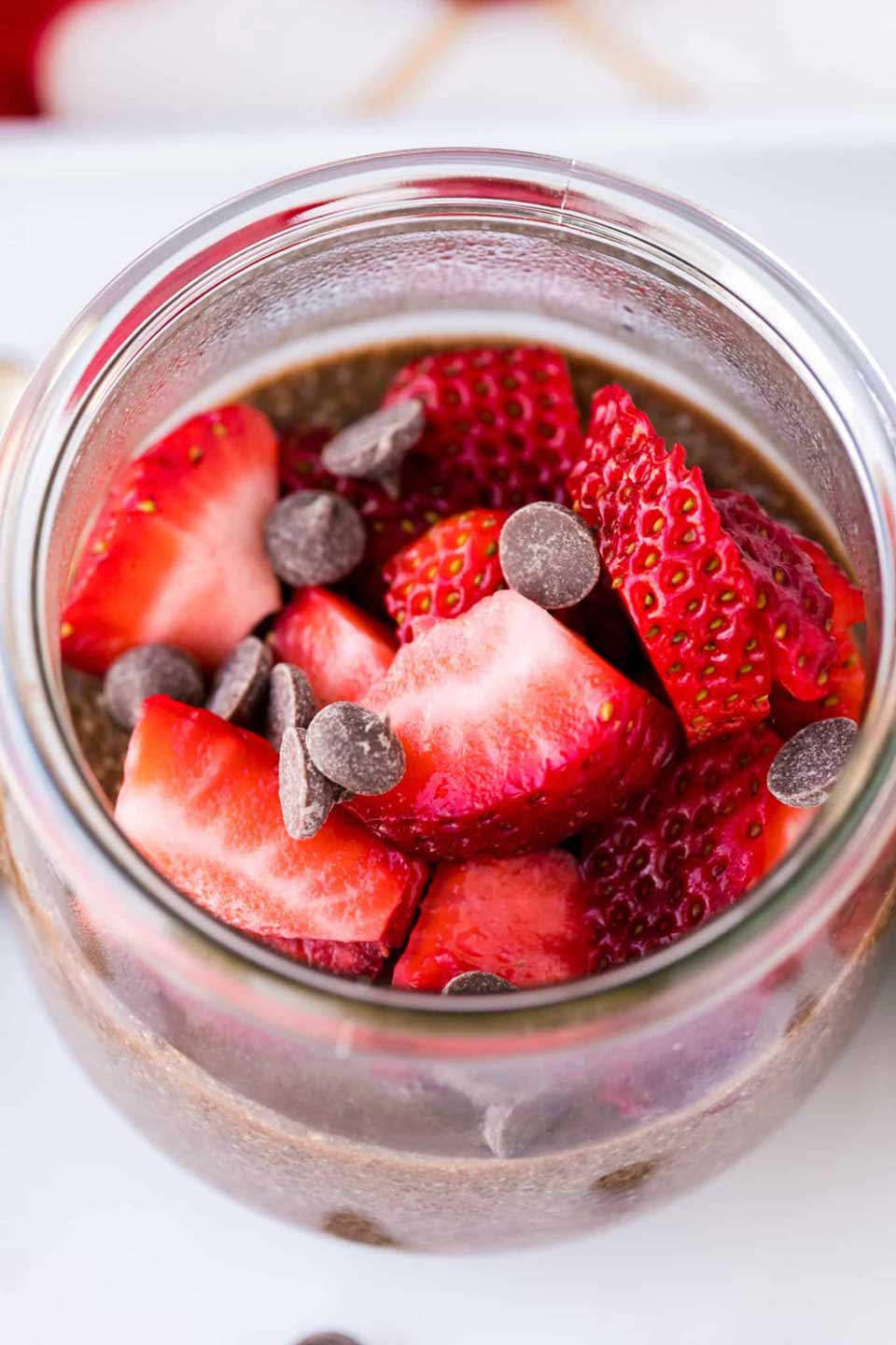 Overhead of this chia pudding in a wide-mouthed jar so you can see the topping of chopped strawberries and chocolate chips.