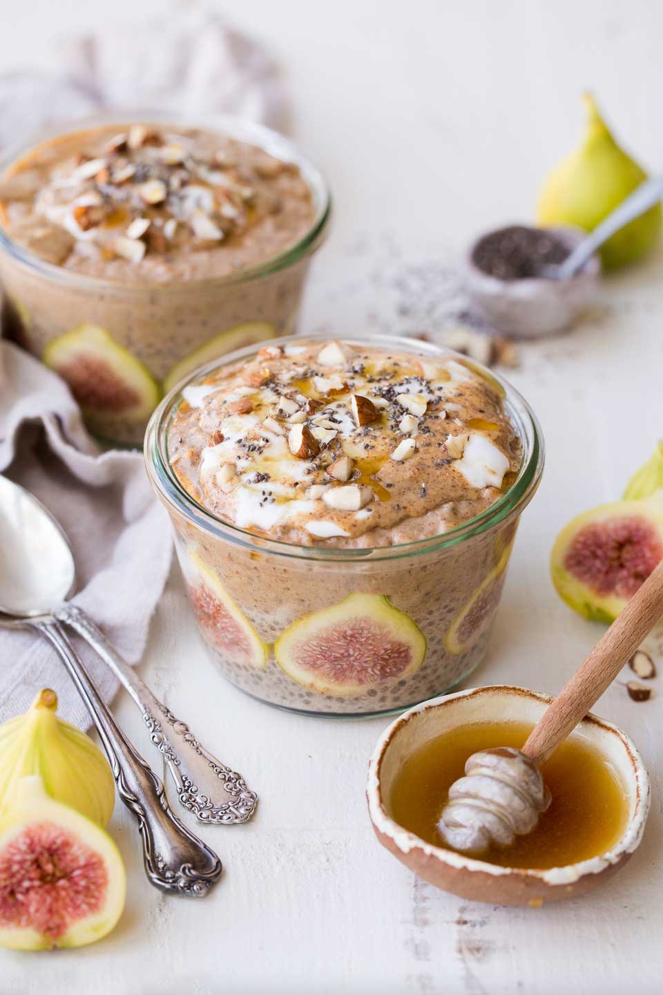 Two squat glass jars of this chia pudding, with cut figs a bowl of honey, and spoons alongside.