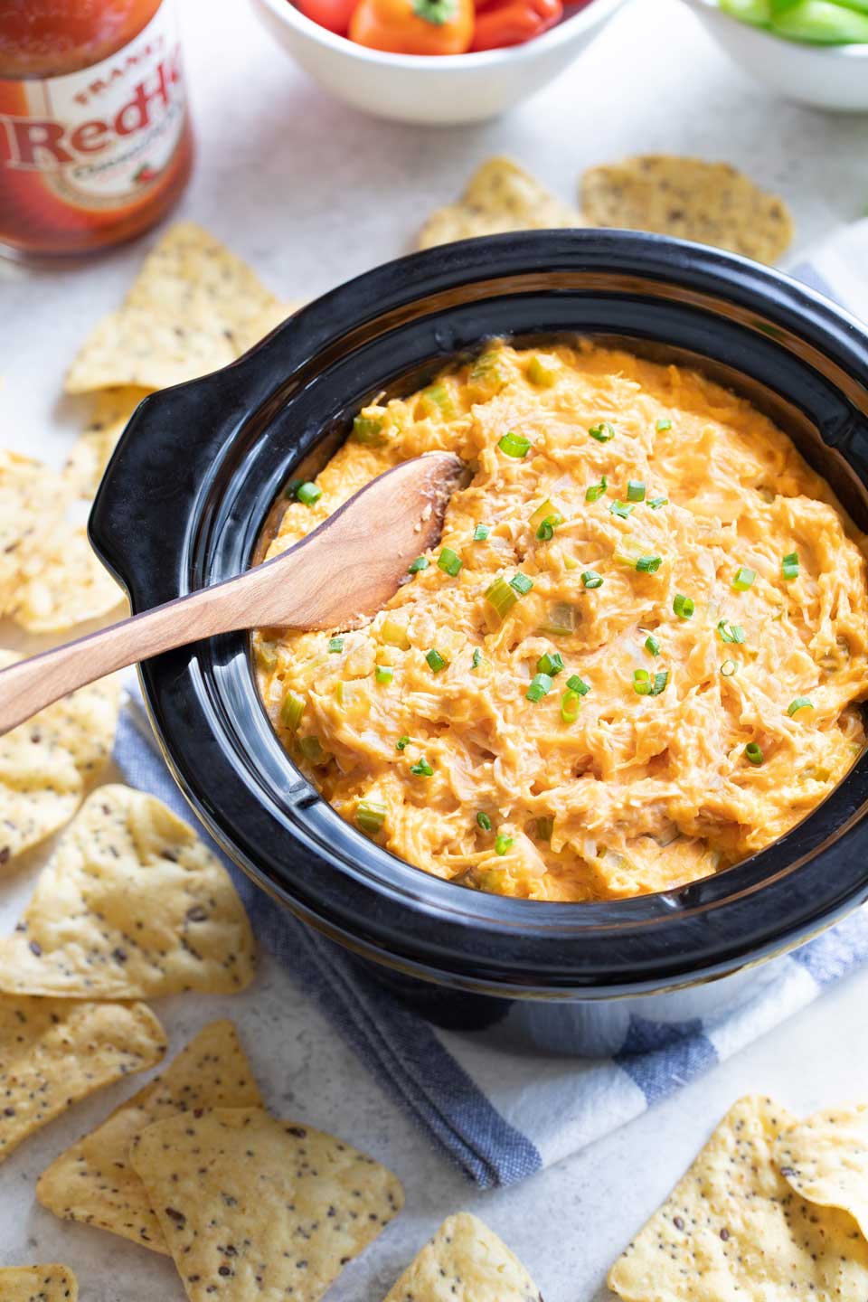 Cooked dip in crockpot insert with Frank's Red Hot Buffalo Chicken Sauce and dippers nearby.