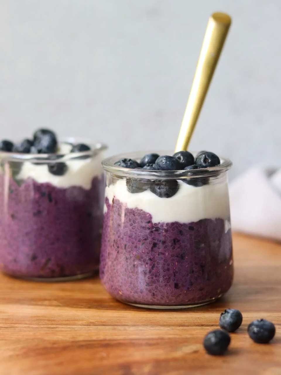Side view of two glass jars of this layered recipe, garnished with blueberries.