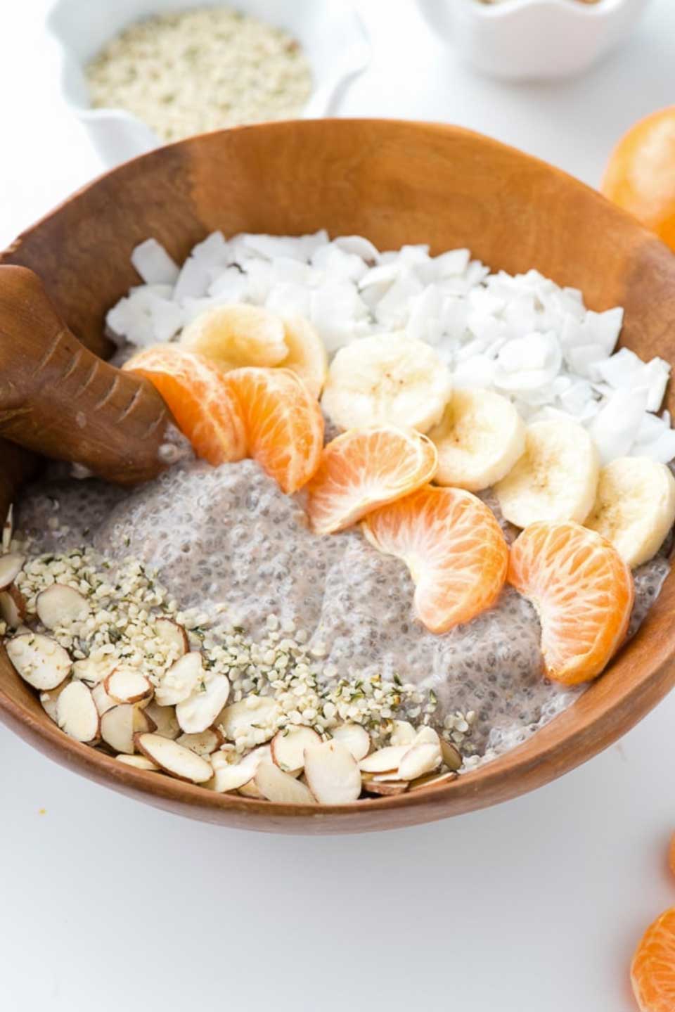 Wooden bowl of chia seed pudding topped with rows of fruit, seeds, nuts and coconut.