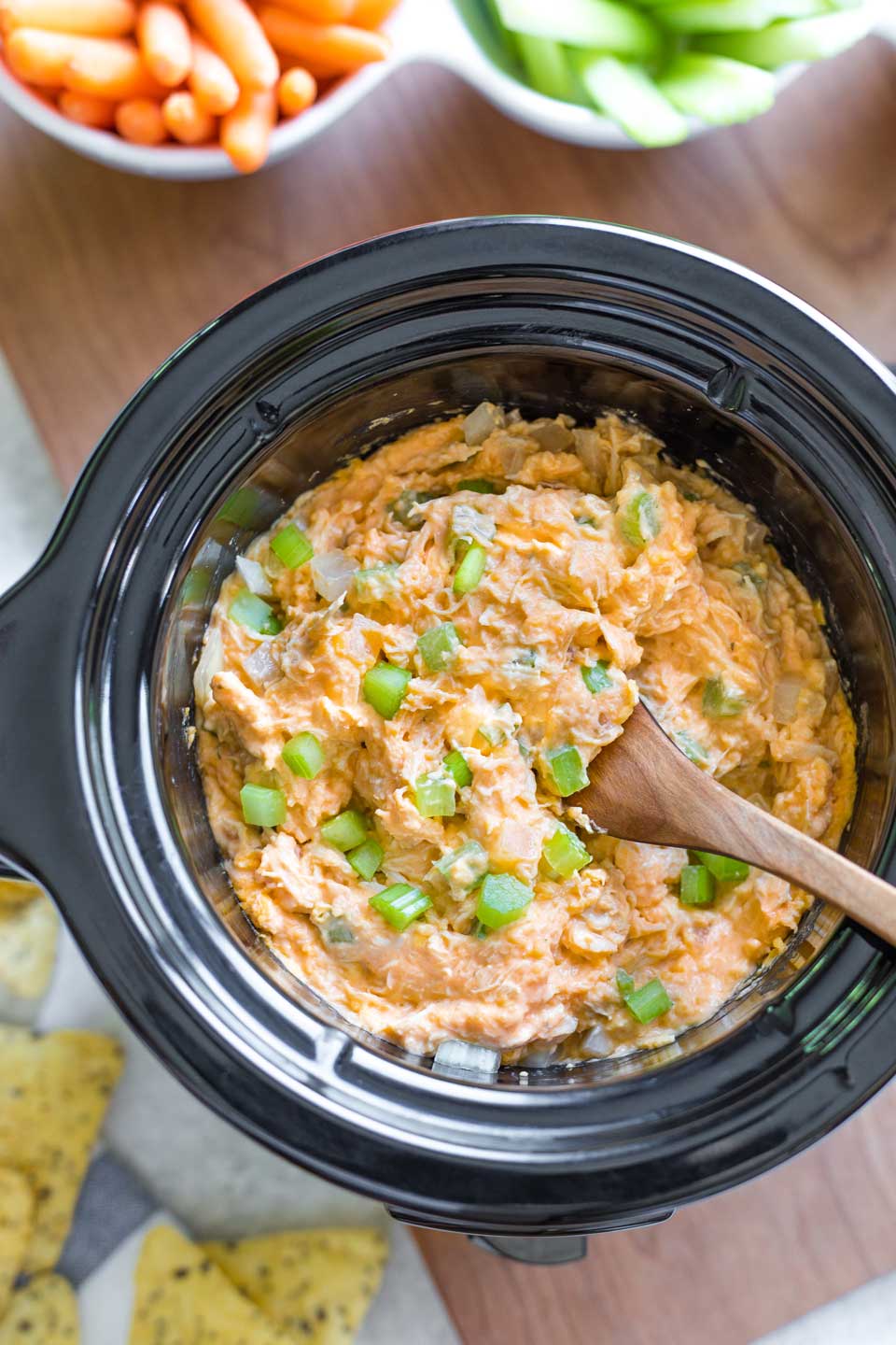 Wooden spoon stirring veggies into cooked buffalo chicken dip.