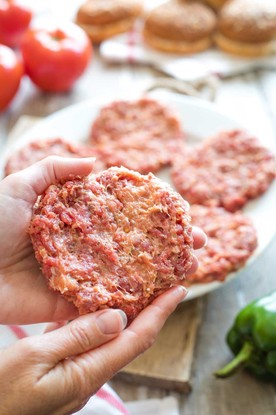 Closeup of two hands shaping a raw Italian hamburger before grilling it.