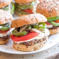 Closeup of one finished burger on a white platter full of burgers.