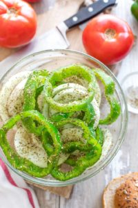 Clear bowl full on slice onions and peppers sprinkled with Italian seasoning.