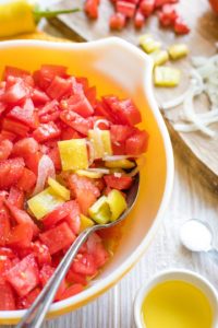 Pieces of tomato and onion and pepper in salad bowl, just being stirred together.