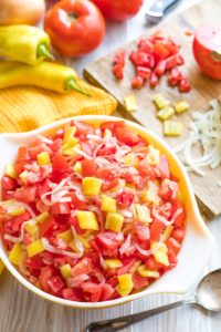 Overhead of full serving bowl of salad, with pieces of tomato and onion plus whole vegetables in background.