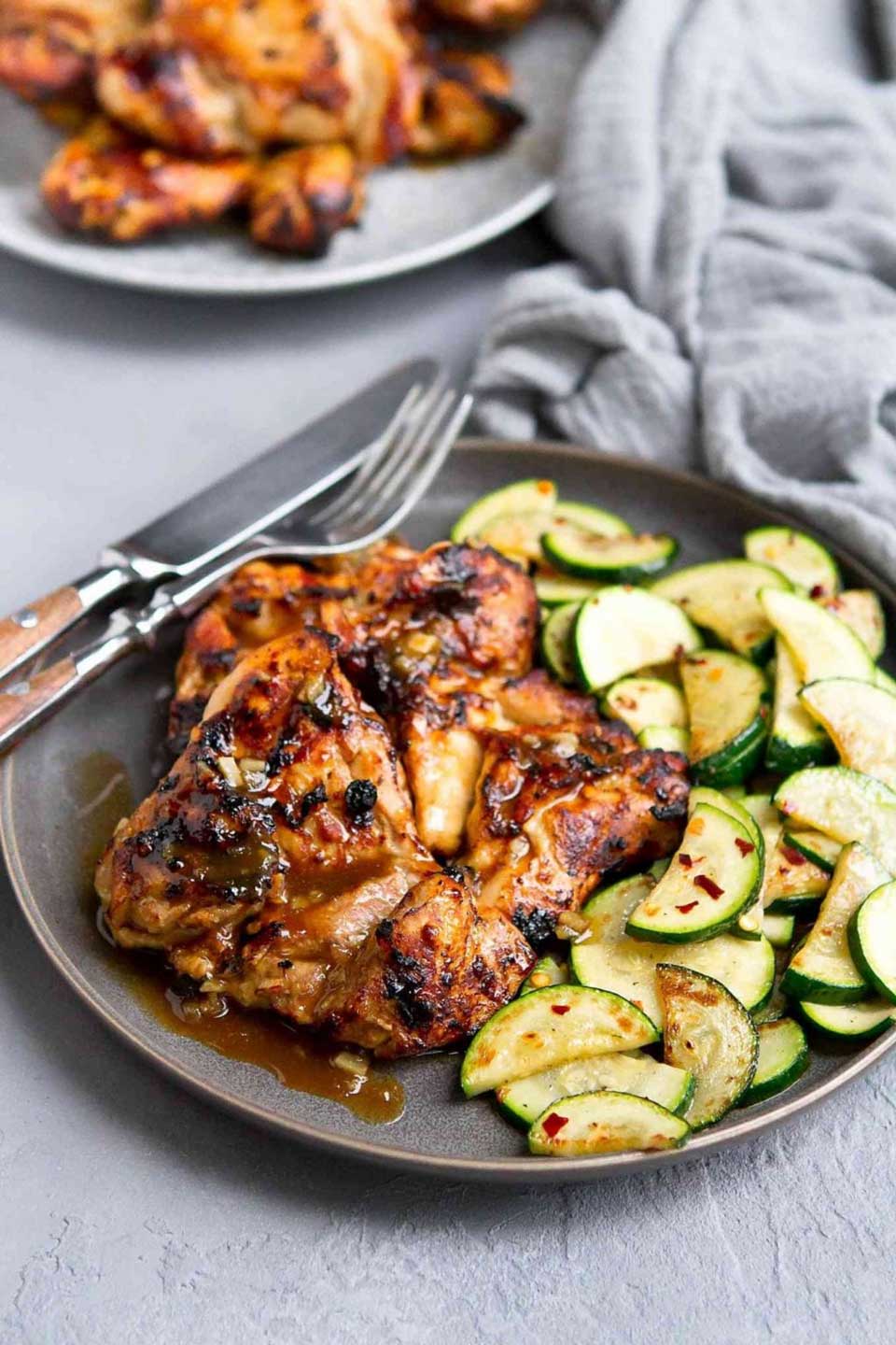 Two honey balsamic thighs on gray plate with sauteed zucchini side dish.
