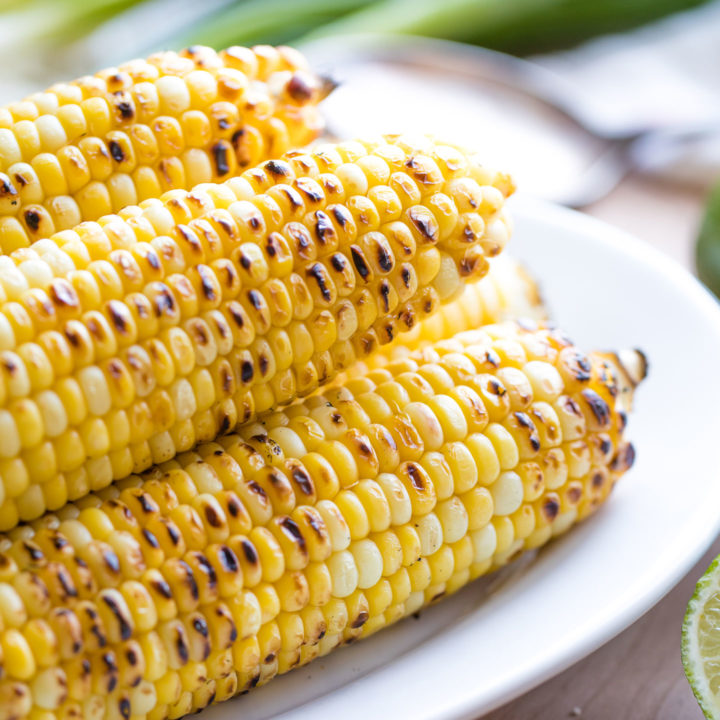 Closeup of grilled corn piled on a serving platter, so you can see the char marks.