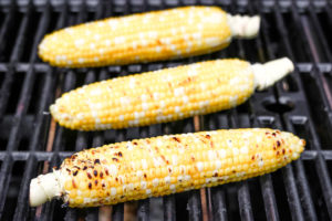 3 ears of corn on the cob on the grill that are almost done cooking, with brown spots visible.