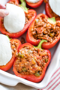 Peppers stuffed in baking dish with hand laying mozzarella on top.