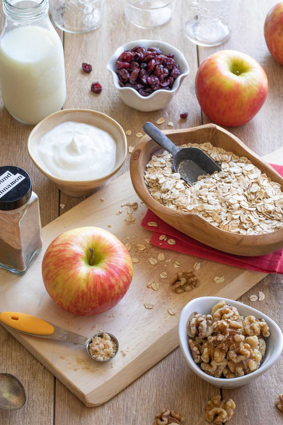 Recipe ingredients like apple oats walnuts milk and cinnamon, in various little bowls on a cutting board.