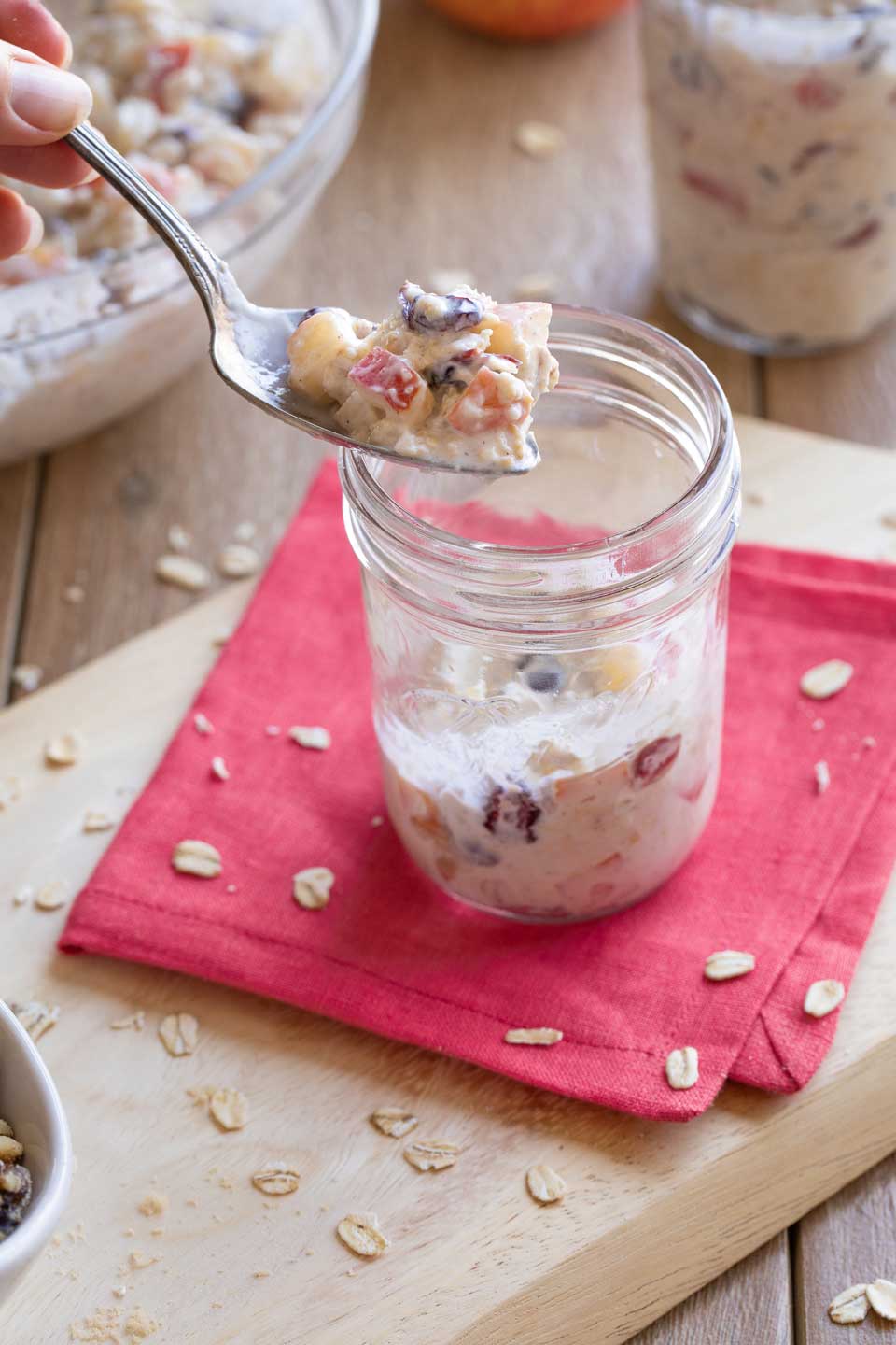 A hand holding a spoon and beginning to fill a meal prep jar with the Overnight Oats.