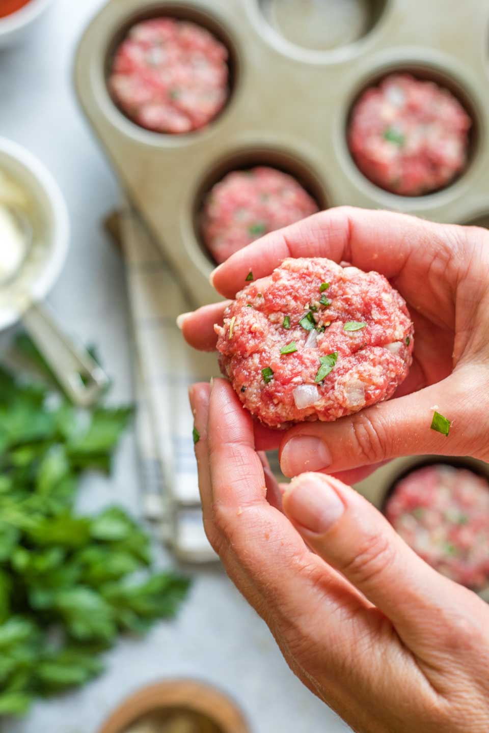 Two hands shaping a mini meatloaf, with more in background below, already nestled in muffin tin.