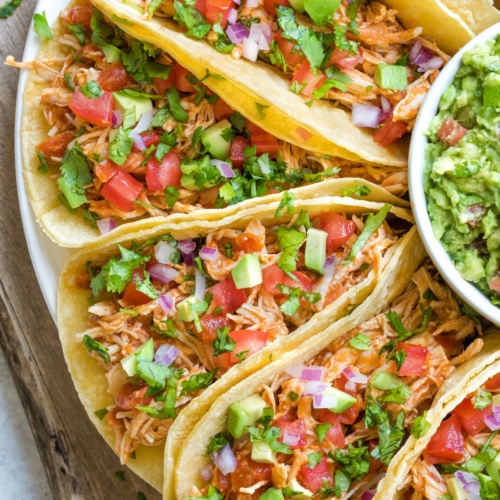 Several tacos loaded with lots of toppings with a side of guac.