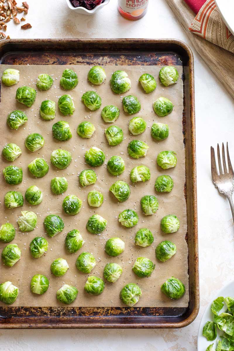 Overhead of sprouts on parchment-lined sheet pan, tossed with oil and seasonings and ready to be roasted.