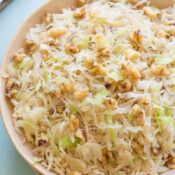 Overhead closeup of tan serving bowl of sauteed cabbage on light blue background and cloth, garnished with extra nuts.