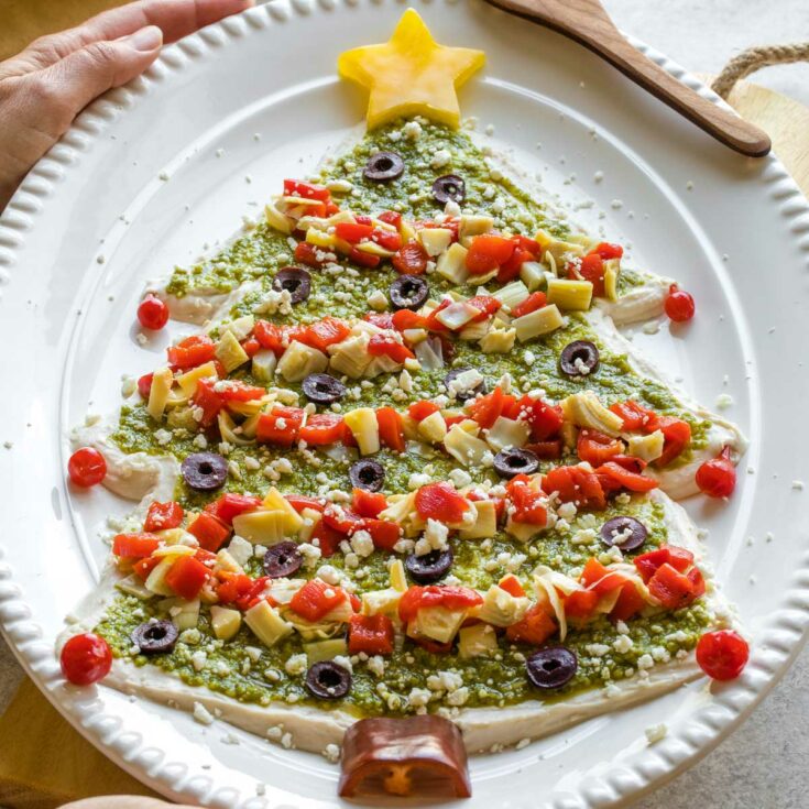 Dip being served by two hands at Christmas party with wooden spreader resting on platter.