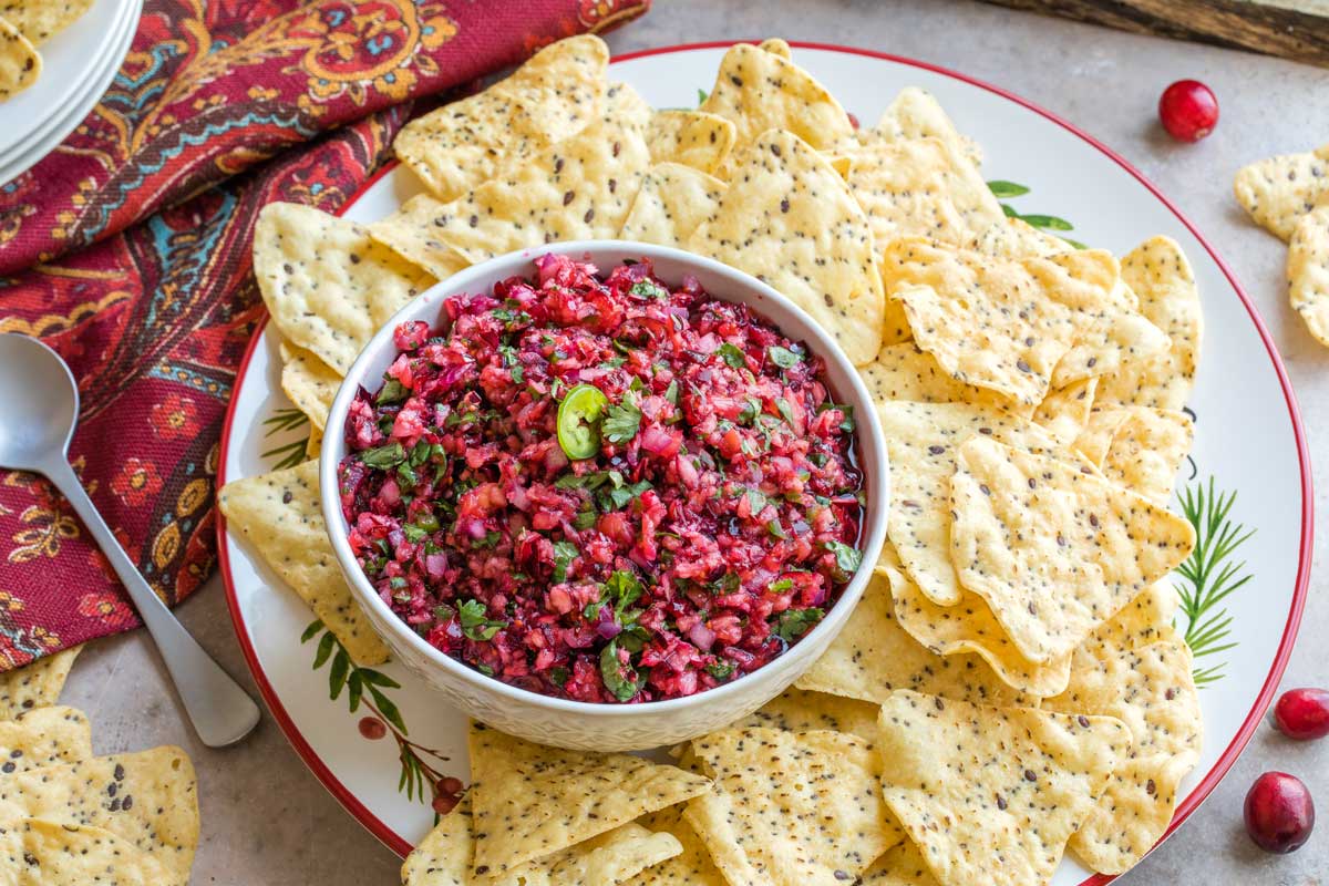 Festive scene with salsa in bowl on a red-rimmed, cranberry-printed platter and nestled amongst tortilla chips.