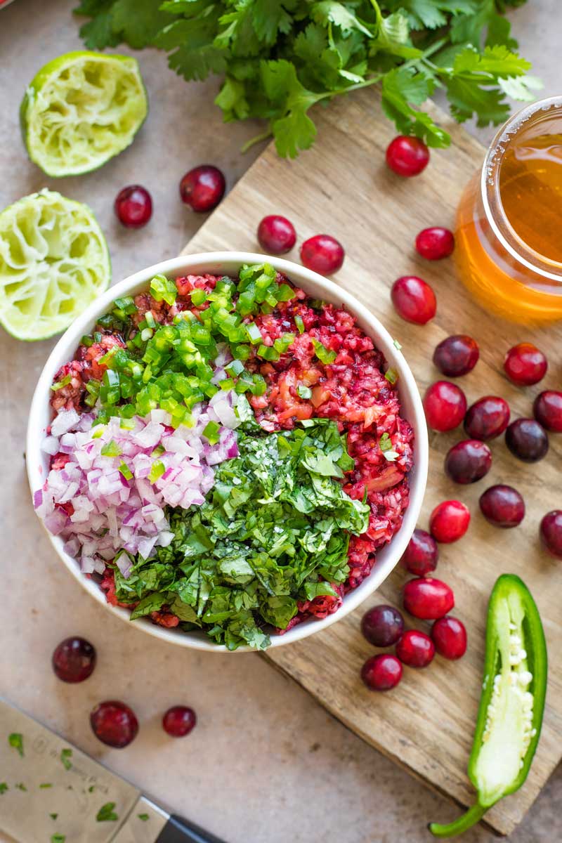 Overhead of bowl filled with cranberry mixture, with chopped onions, jalapeno and onion arranged on top and waiting to be mixed into the salsa.
