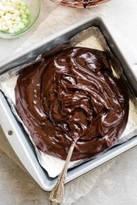 Mint chocolate mixture poured into foil-lined fudge pan with a spoon beginning to smooth it out.