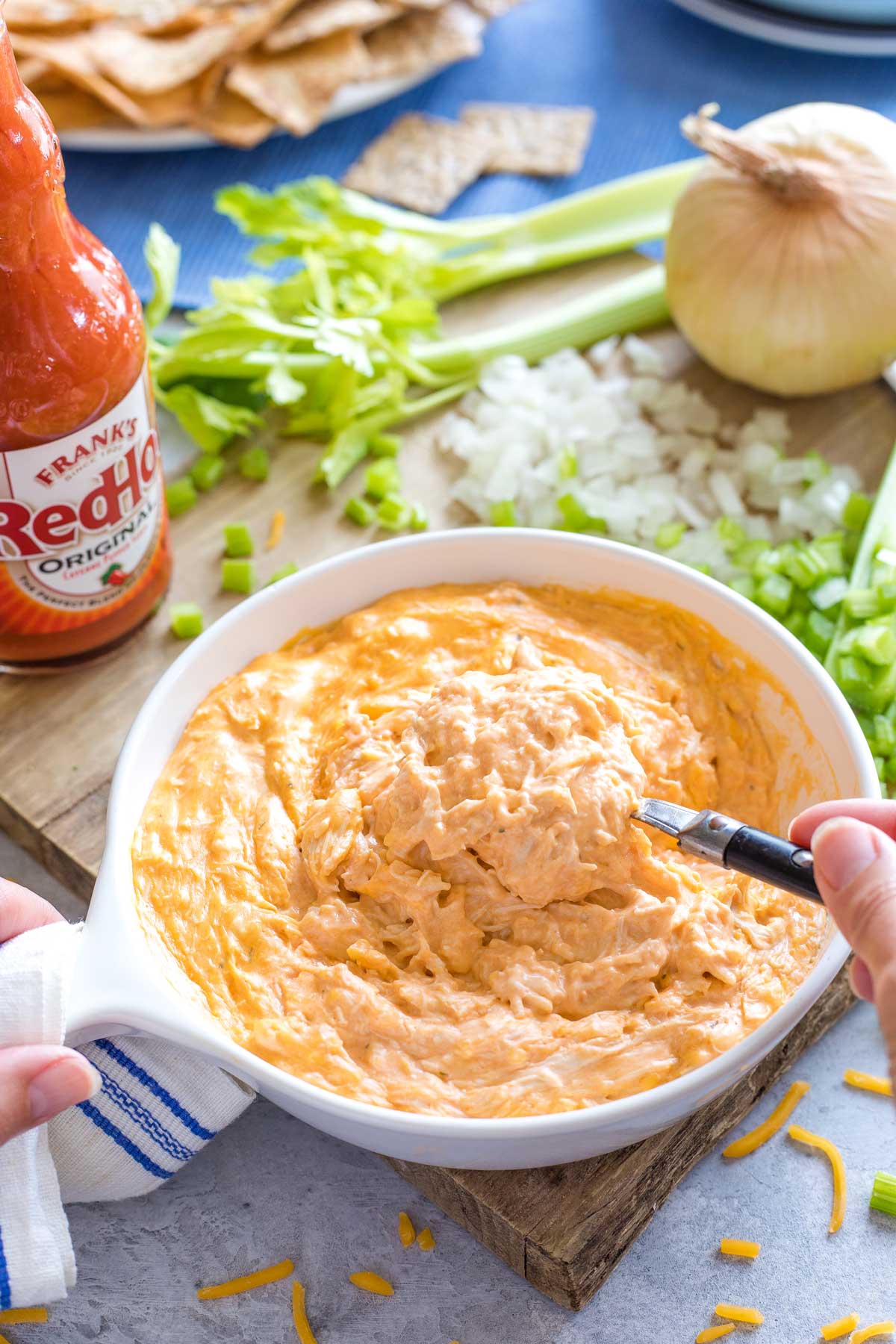 Hands stirring together hot, melty Buffalo Dip before veggies are added.