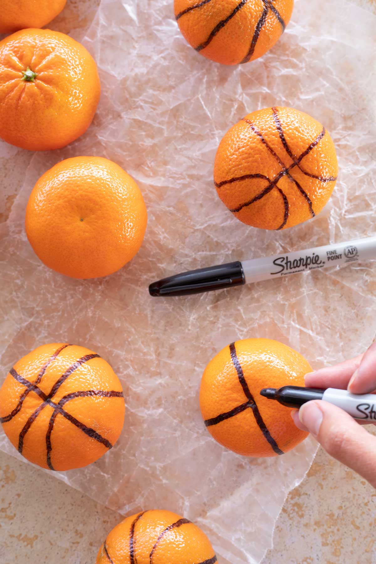 Fingers holding Sharpie to draw lines on clementine to look like a basketball.