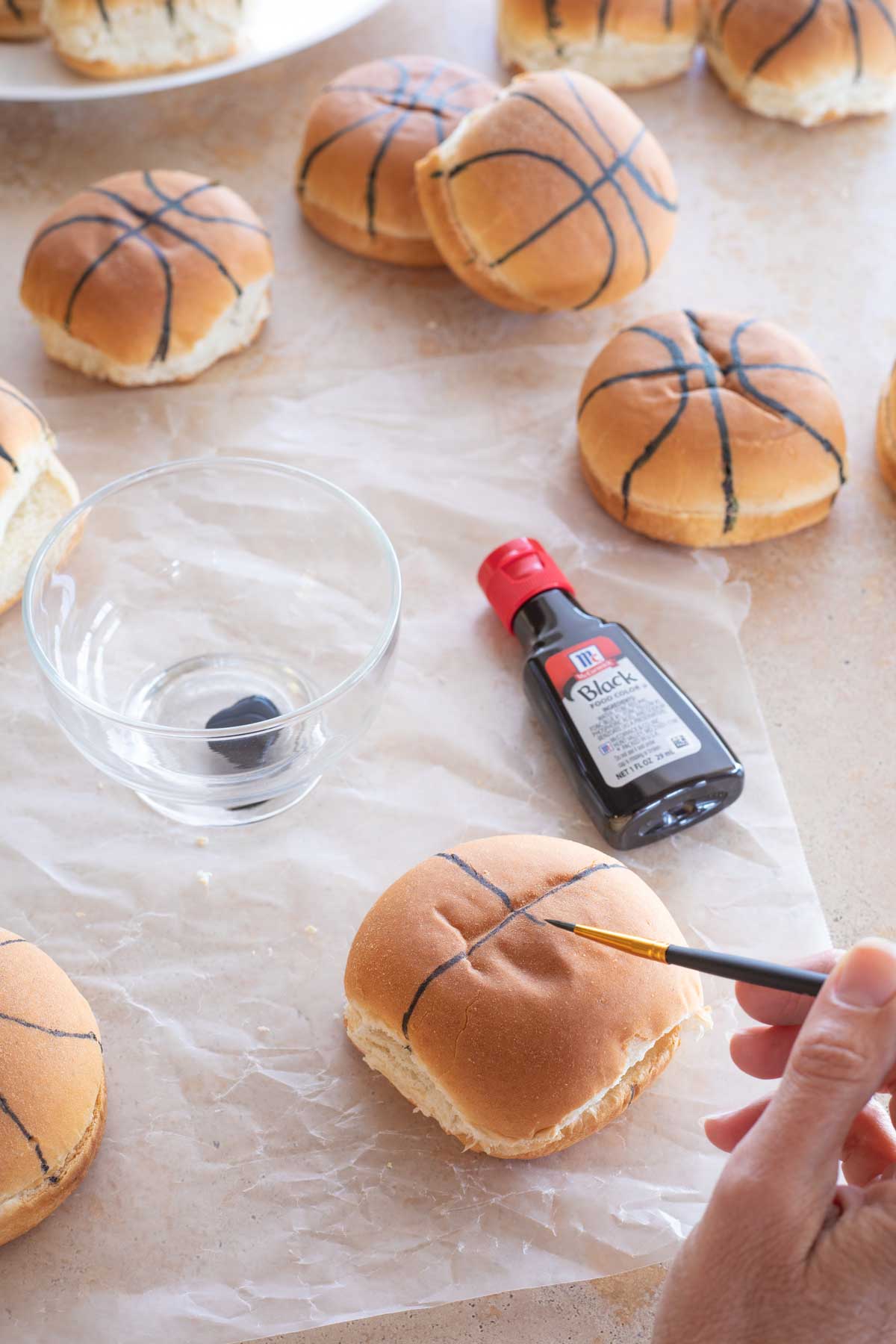 Hand using paint brush and food coloring to make a bun look like a basketball.