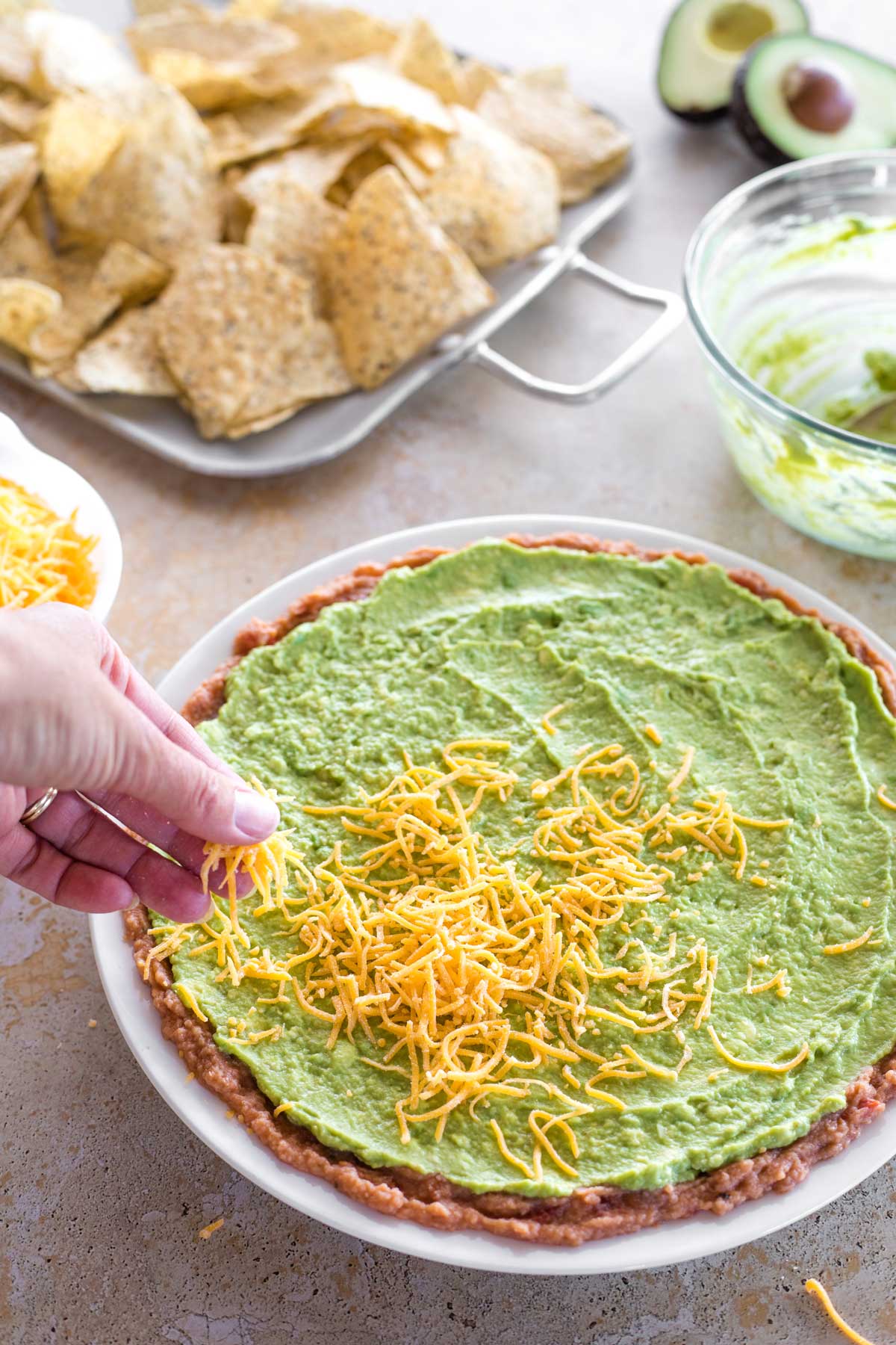 Hand sprinkling cheese on top of guacamole layer.
