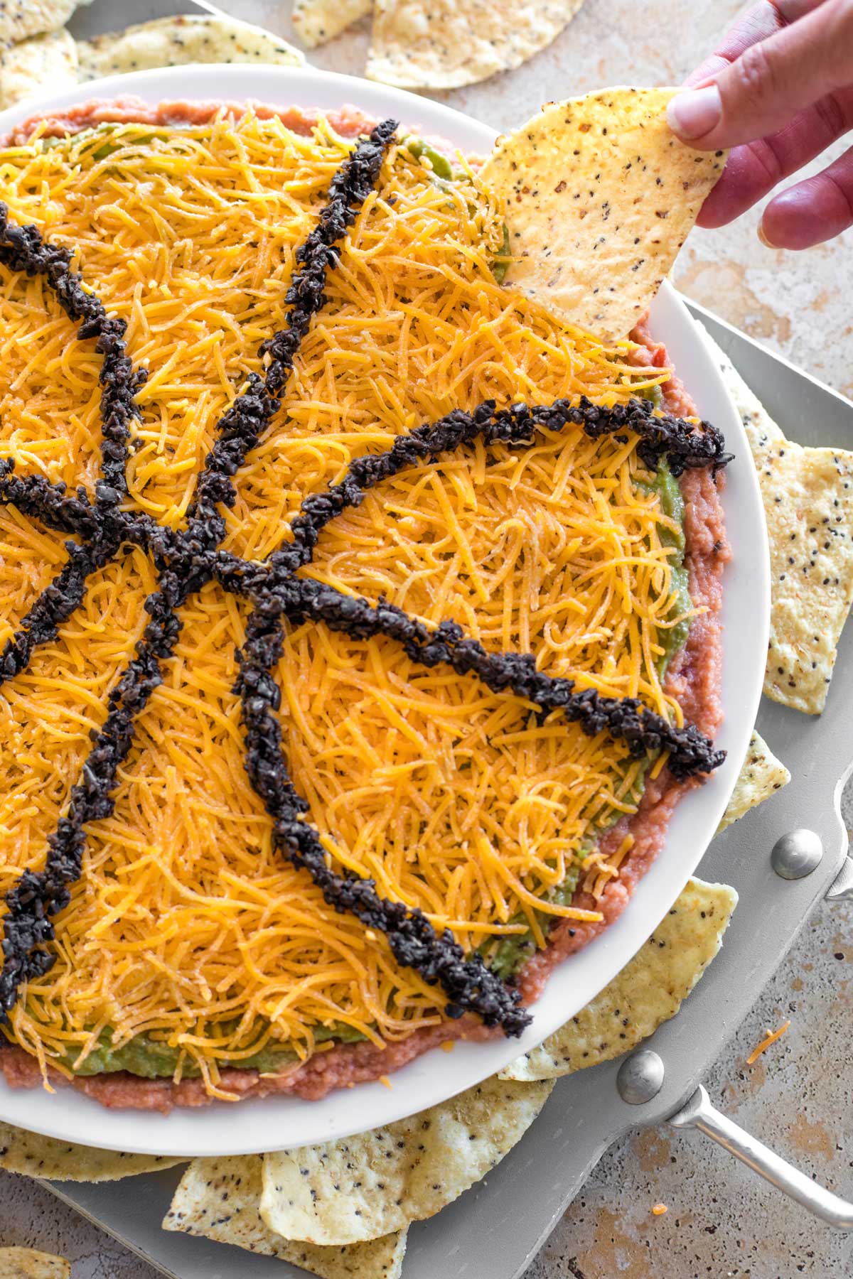 Fingers dipping tortilla chip in basketball-shaped layered dip.