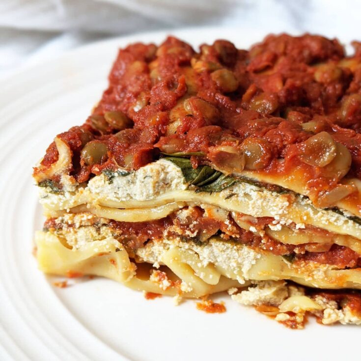 Closeup of the side of one slice of vegan lasagna on a white plate.