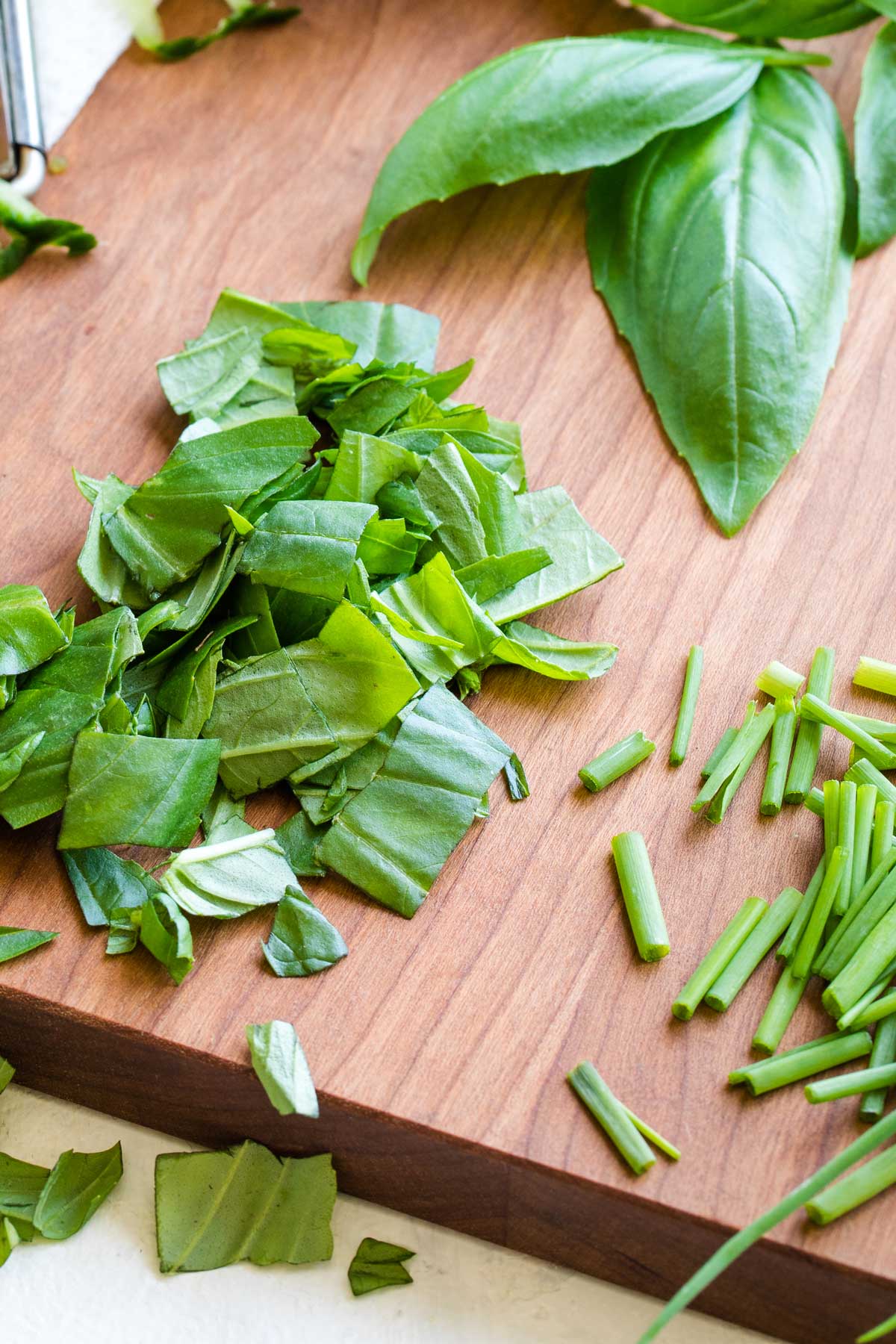 Whole basil leaves, a pile of chopped basil, and a little pile of sliced chives on a cutting board.