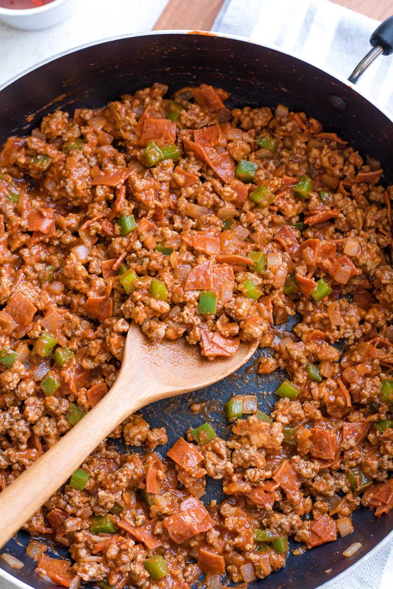 Overhead of fully cooked sloppy joe mixture in skillet with wooden spoon dipped in.