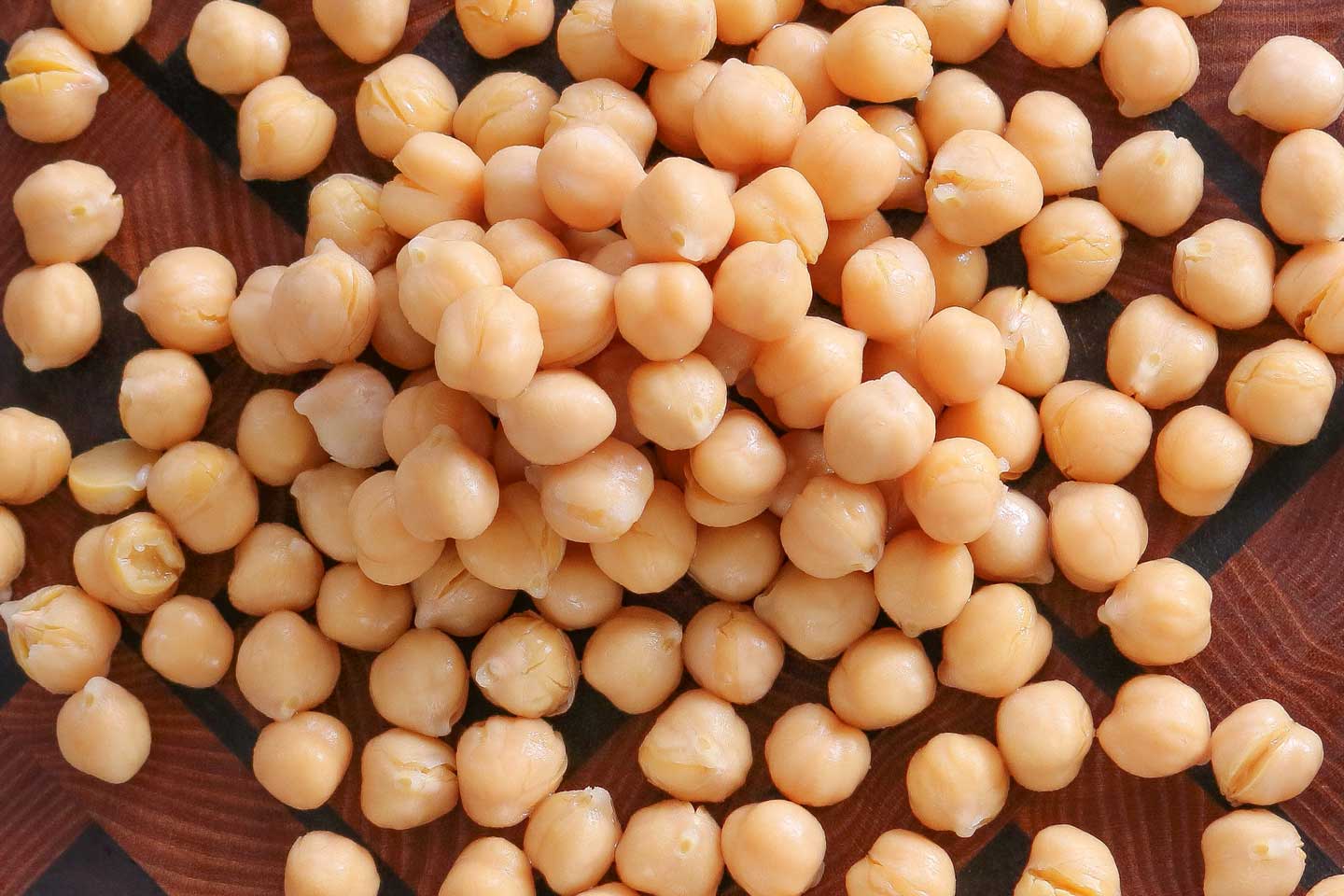Closeup overhead of a pile of chickpeas on a wooden cutting board.